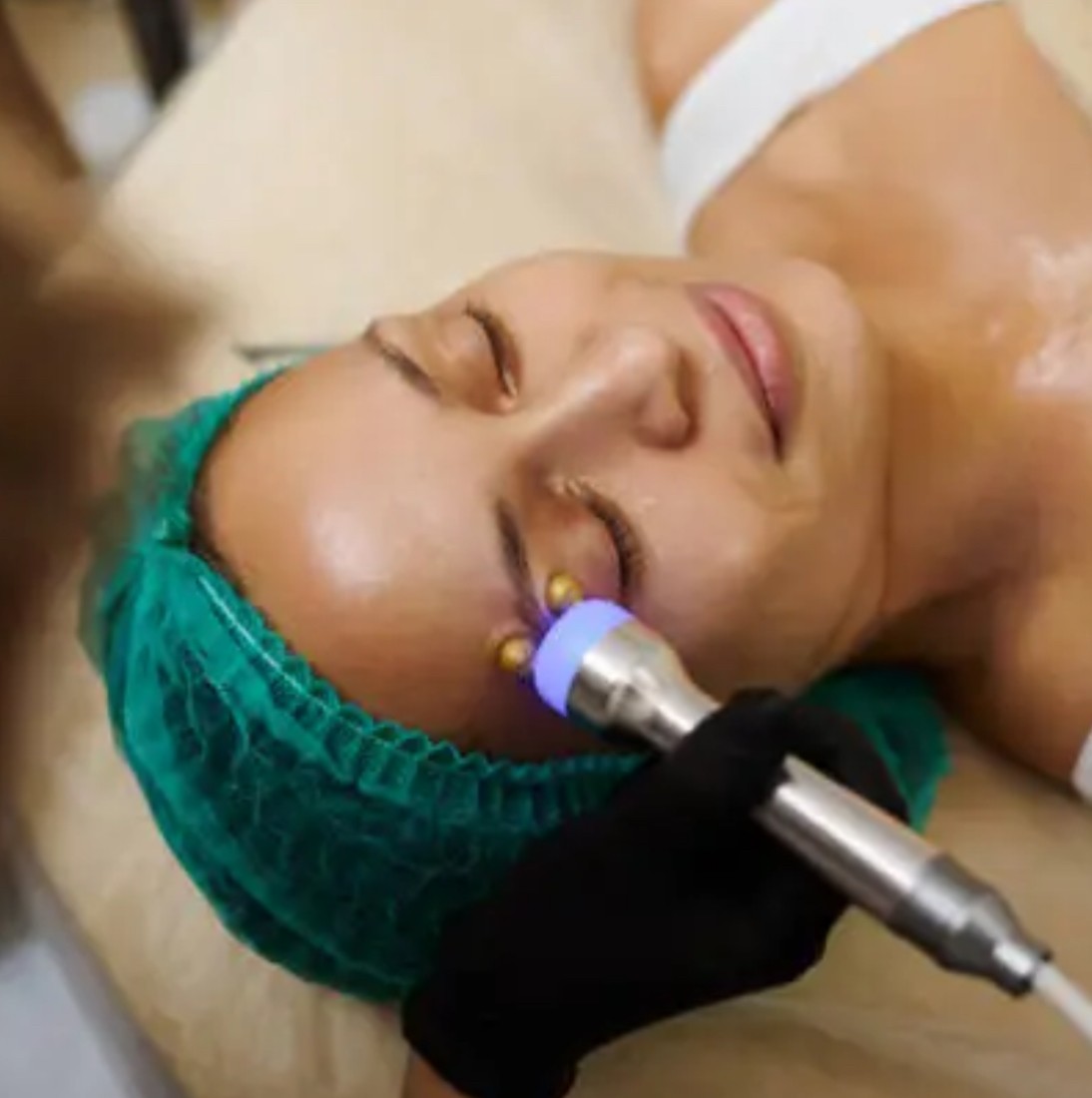 Woman receiving a facial treatment with a handheld device emitting blue light applied near her closed eye.
