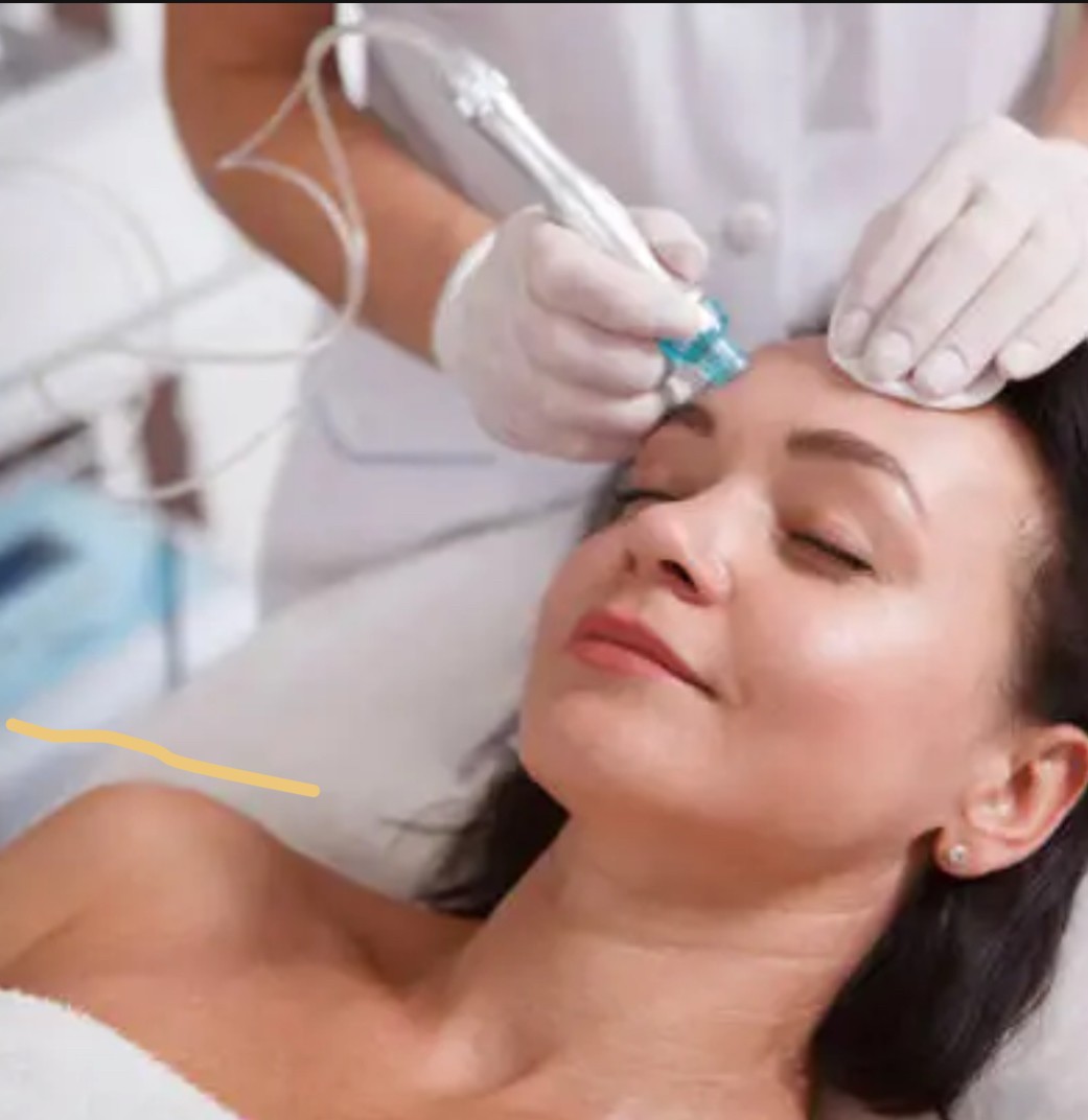 Woman receiving a hydrafacial treatment with a handheld device on her forehead by a professional wearing gloves.