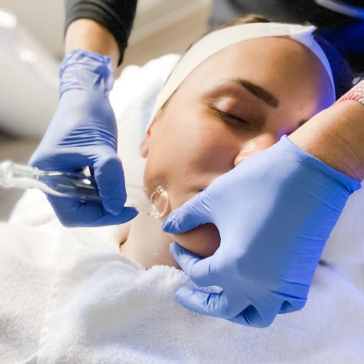 Person receiving a facial treatment with a glass suction device held by hands wearing blue gloves.