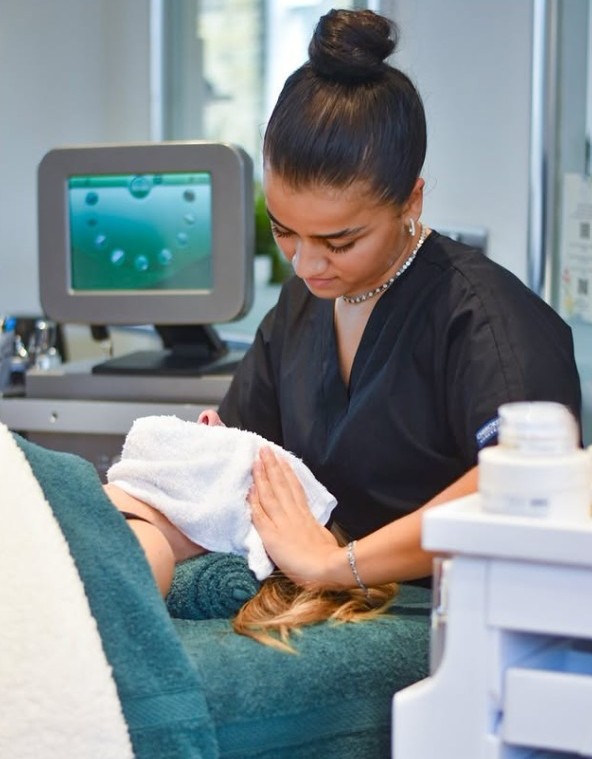 Woman in black uniform gently wiping a client's face with a towel during a spa treatment.