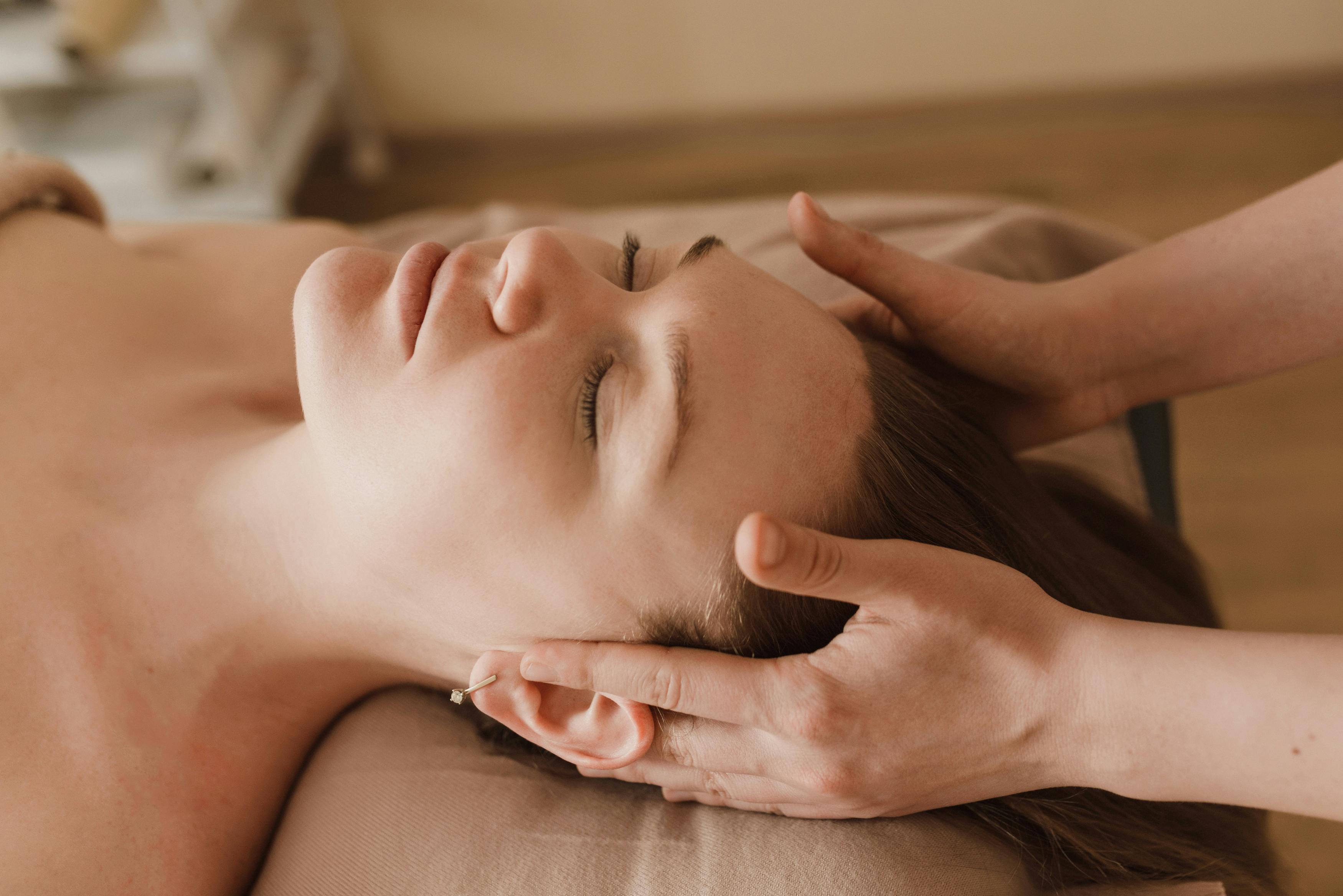Person receiving a gentle head massage with eyes closed, lying on a massage bed.